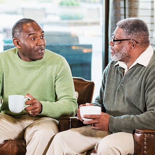 Two African-American men sitting on a sofa talking over coffee