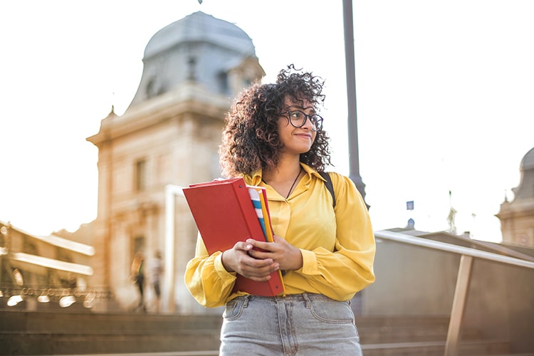 Young woman standing outside holding books