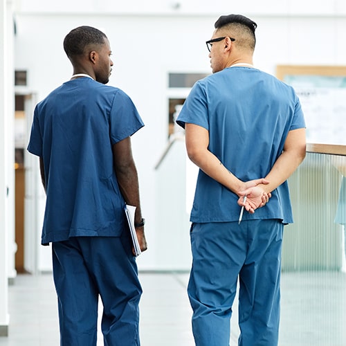 Two doctors wearing blue uniform walking in hall of modern clinic