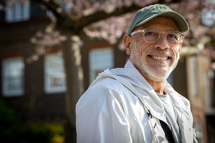 Older man smiling and wearing a baseball cap, glasses and jacket